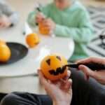 Family enjoys creative Halloween activity by painting oranges indoors, bonding and having fun together.
