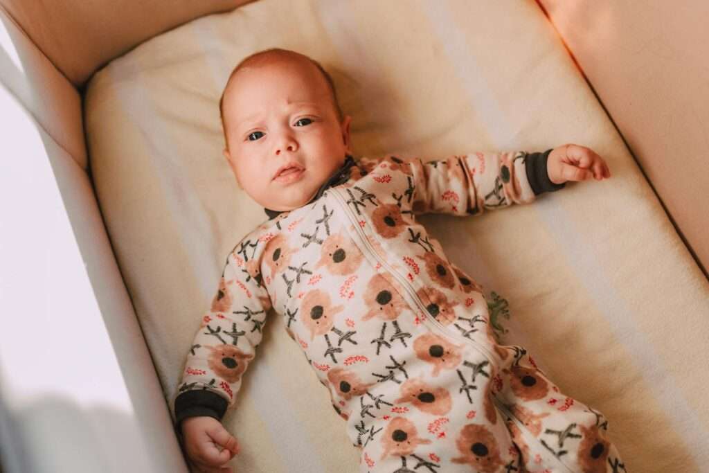 Cute baby boy in floral pajamas lying on a cushion in a crib, top view