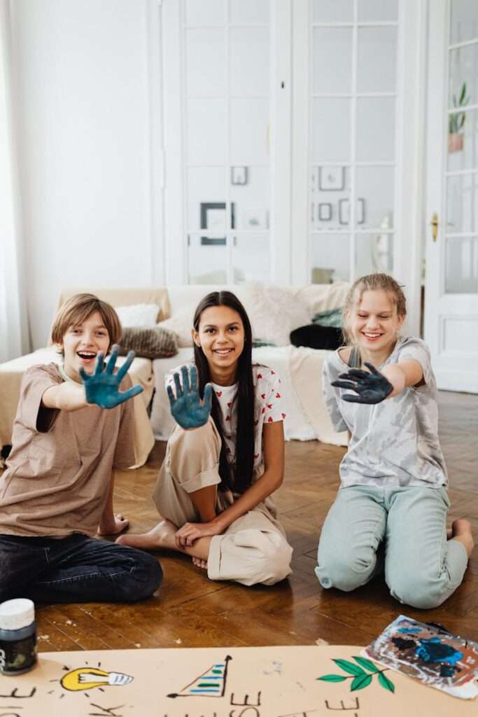 Three smiling teens enjoying a fun art project with paint in a bright indoor space.