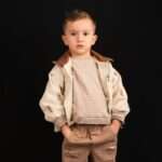 Young boy in stylish outfit stands against black background