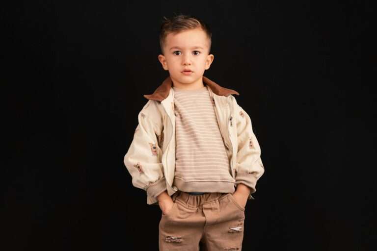 Young boy in stylish outfit stands against black background