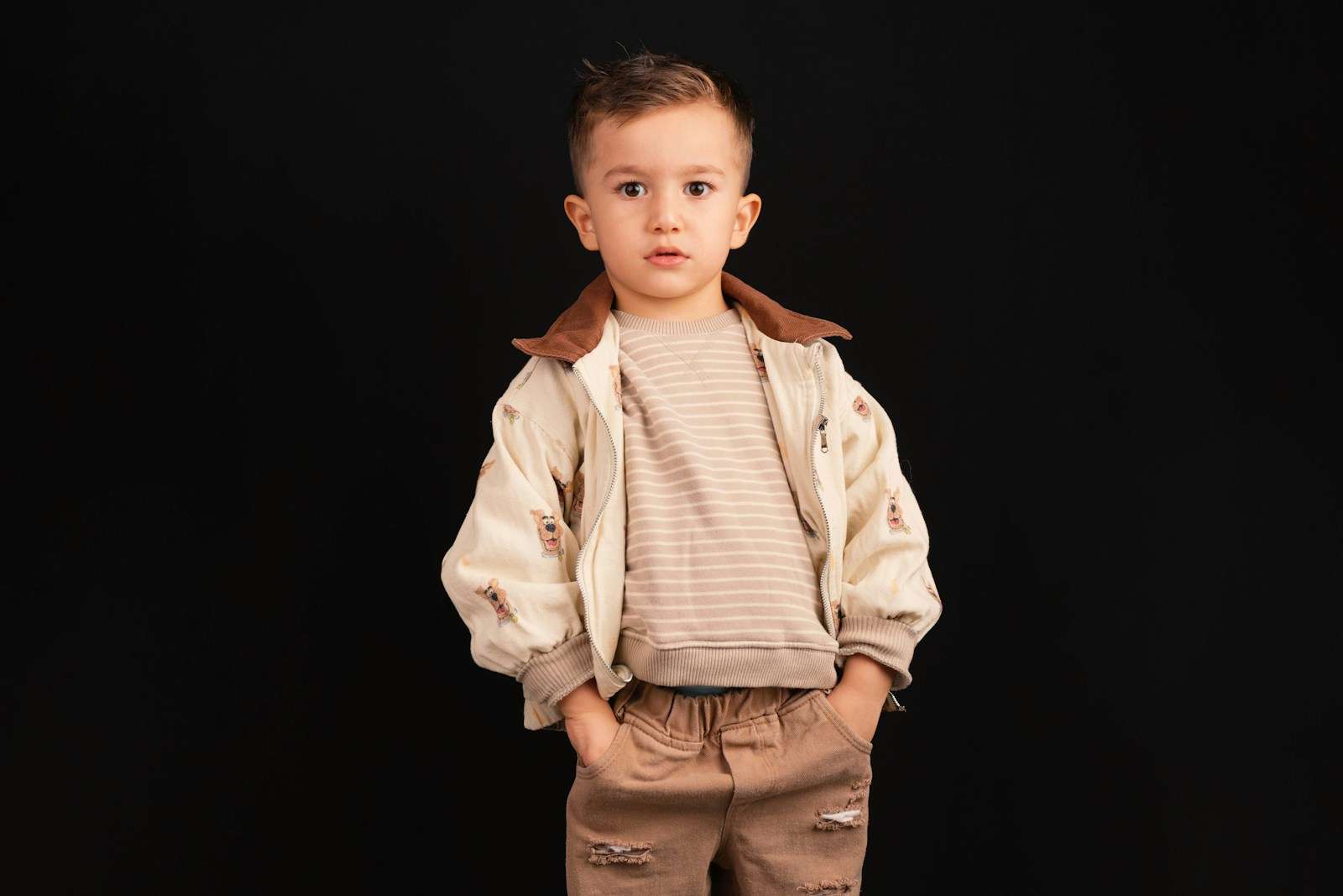 Young boy in stylish outfit stands against black background